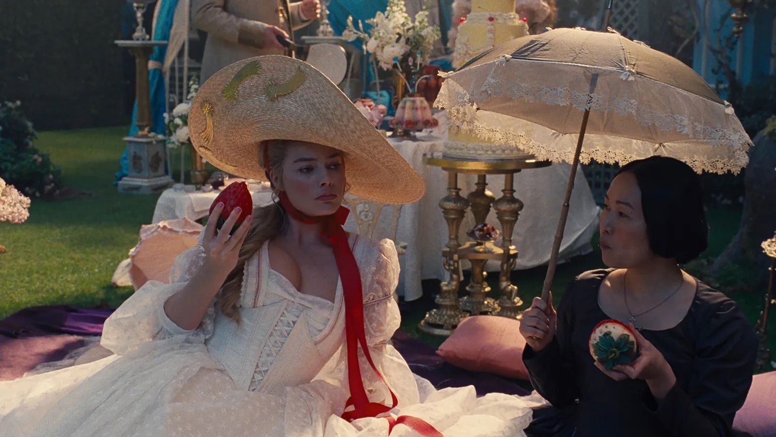 Margot Robbie and Hong Chau eating giant strawberries in Wuthering Heights